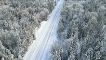 Aerial Clip Looking Down Onto A Winter Snow-covered Forest And Rural Road. The Forest Is Made Up Of Mixed Evergreen And Deciduous Trees.  The Drone Is Moving Forward.
