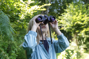 Cute little girl exploring nature looking through binoculars. Child playing outdoors. Kids travel, adventure and bird watching concept.