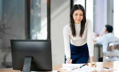 Successful Young Businesswoman standing at Her Desk Working on document and desktop Computer.