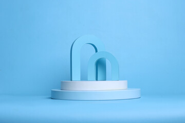 Minimal composition of two archs on white cylinder podium on blue color pastel background. Display and showcase for cosmetic product