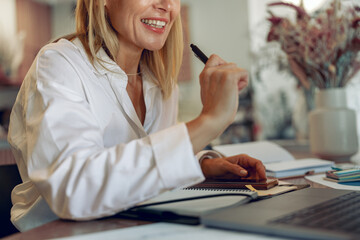 Wall Mural - Close up of smiling business woman working on laptop, making notes in cozy coworkign space interior