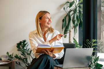 Wall Mural - Smiling woman manager working on laptop, making notes in cozy coworkign space interior