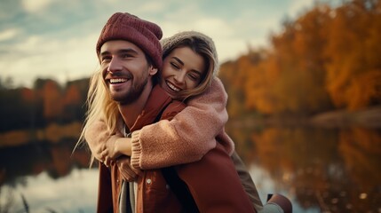 Lovely couple having fun together in nature. Fashion couple enjoying autumn. Boyfriend carrying his girlfriend on piggyback.Young couple walking near lake in autumn