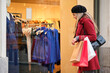 © Ladanifer - Young caucasian blonde woman holding shopping bags looking at store window in winter.