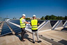Two Technicians Discussing Plan On The Roof Of A Company Building With Solar Panels