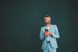 © Westend61 - Thoughtful businessman with smart phone standing against teal background