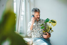 Businessman Talking On Smart Phone Holding Plant At Office