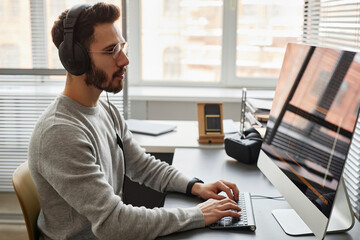 Computer programmer wearing headphones working on desktop PC in office