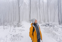 Happy young caucasian woman in yellow jacket enjoying walk under snowfall in winter forest