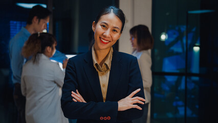 Wall Mural - Portrait of successful executive businesswoman smart casual wear looking at camera and smiling, happy in modern night office workplace. Young Asia lady standing relax in contemporary meeting room.