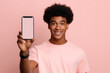 Happy African American teen student holding mobile cell phone pointing finger at smartphone mock up big screen template presenting application, using cellphone showing ad isolated on beige background.