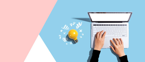 Wall Mural - Person using a laptop computer and a light bulb - Flat lay