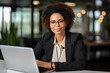 © AI_images - Young happy professional African American business woman wearing suit eyeglasses working on laptop in office sitting at desk looking at camera, female company manager executive portrait at workplace
