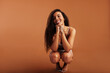 © Flamingo Images - Young black woman in underwear smiling while crouching on an orange background