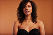© Flamingo Images - Young black woman wearing a strapless bra against an orange background