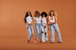 © Flamingo Images - Diverse women in jeans and white tops standing on an orange background and laughing