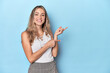 © Asier - Blonde young caucasian woman in blue studio excited pointing with forefingers away.