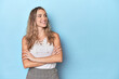 © Asier - Blonde young caucasian woman in blue studio smiling confident with crossed arms.