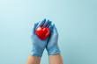 Heart disease prevention concept. Top view photograph of hands in medical gloves holding a heart model on light blue isolated background with copy-space for text or advertising placement