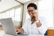 © Vadim Pastuh - Confident young entrepreneur using laptop, talking on mobile phone in contemporary co-working space. Stylish african-american woman with short haircut sitting at desk, has pleasant phone conversation
