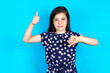 Caucasian kid girl wearing floral dress over blue background  showing thumbs up and thumbs down, difficult choose concept