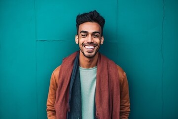 Wall Mural - Portrait of a happy young indian man standing against blue wall