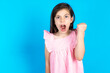 caucaisna kid girl wearing pink dress over blue background angry and mad raising fist frustrated and furious while shouting with anger. Rage and aggressive concept.