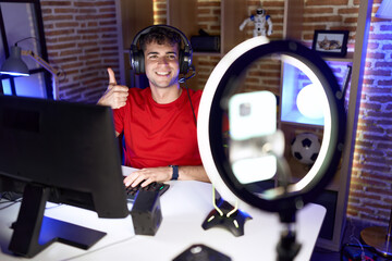 Sticker - Young hispanic man playing video games recording with smartphone smiling happy and positive, thumb up doing excellent and approval sign