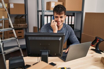 Poster - Young hispanic man ecommerce business worker using laptop talking on smartphone at office