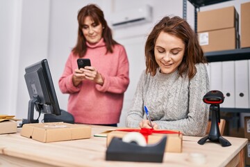 Poster - Two women ecommerce business workers writing on notebook using smartphone at office