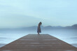 lonely woman standing on a pier by the sea gets carried away by emotions in a blue surreal atmosphere