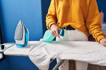 Poster - Young blonde woman ironing clothes applying liquid on t shirt at laundry room