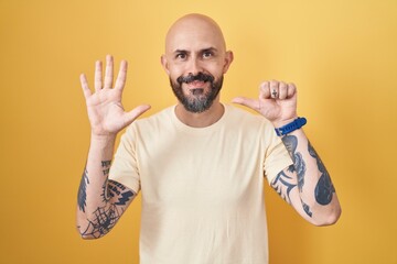 Wall Mural - Hispanic man with tattoos standing over yellow background showing and pointing up with fingers number six while smiling confident and happy.