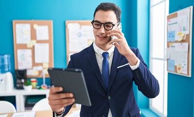 Sticker - Young hispanic man business worker talkiong on smartphone using touchpad at office