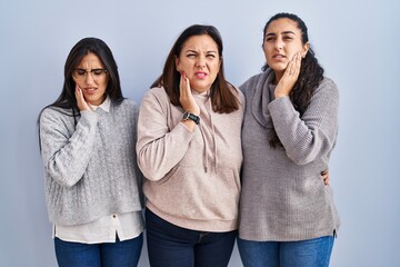 Canvas Print - Mother and two daughters standing over blue background touching mouth with hand with painful expression because of toothache or dental illness on teeth. dentist concept.