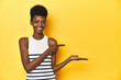 © Asier - Vibrant African woman, white tank-top, yellow studio, excited holding a copy space on palm.