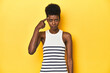 © Asier - Vibrant African woman, white tank-top, yellow studio, pointing temple with finger, thinking, focused on a task.