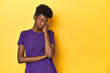 © Asier - African woman in violet tee, yellow studio scene, who feels sad and pensive, looking at copy space.