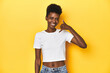 © Asier - African woman, white tee, short hair, yellow studio, showing a mobile phone call gesture with fingers.