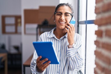 Sticker - Young beautiful hispanic woman business worker talking on smartphone using touchpad at office