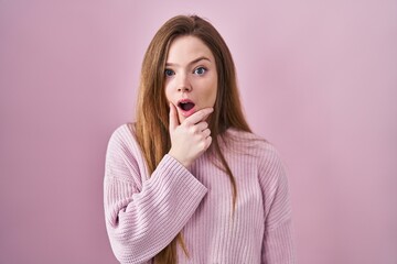 Poster - Young caucasian woman standing over pink background looking fascinated with disbelief, surprise and amazed expression with hands on chin