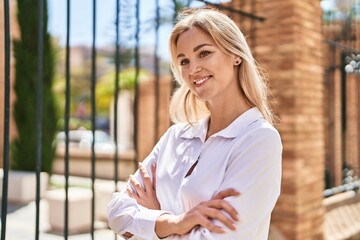 Wall Mural - Young blonde woman smiling confident standing with arms crossed gesture at street