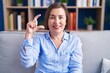 © Krakenimages.com - Middle age hispanic woman sitting on the sofa at home smiling and confident gesturing with hand doing small size sign with fingers looking and the camera. measure concept.