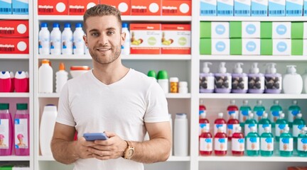 Wall Mural - Young caucasian man customer smiling confident using smartphone at pharmacy