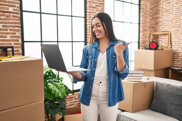 Wall Mural - Hispanic woman using laptop at new home pointing thumb up to the side smiling happy with open mouth