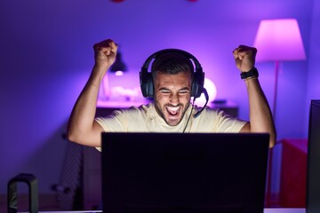 Wall Mural - Young hispanic man streamer playing video game with winner expression at gaming room