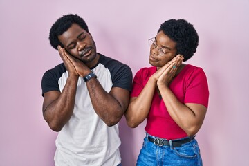 Canvas Print - Young african american couple standing over pink background sleeping tired dreaming and posing with hands together while smiling with closed eyes.