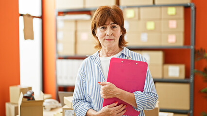 Poster - Middle age woman ecommerce business worker holding clipboard at office