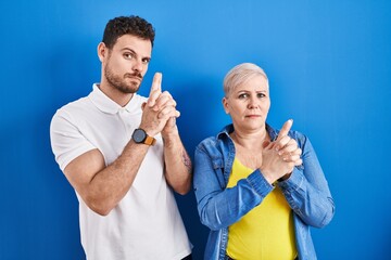 Sticker - Young brazilian mother and son standing over blue background holding symbolic gun with hand gesture, playing killing shooting weapons, angry face