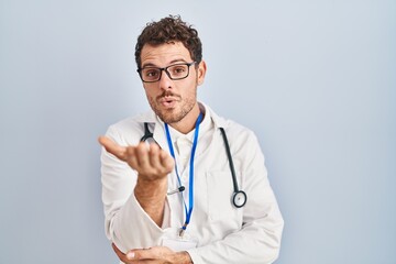 Wall Mural - Young hispanic man wearing doctor uniform and stethoscope looking at the camera blowing a kiss with hand on air being lovely and sexy. love expression.